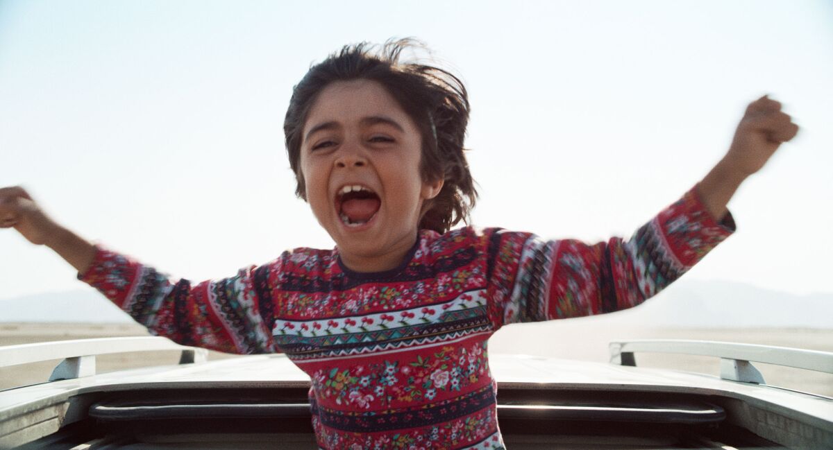A child raises his arms in delight from a car's sun roof.
