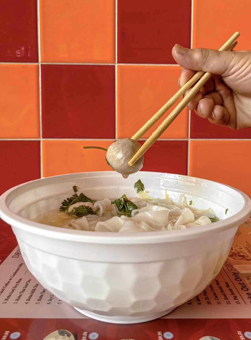Closeup of a large bowl of soup with a hand holding chopsticks with a piece of food.