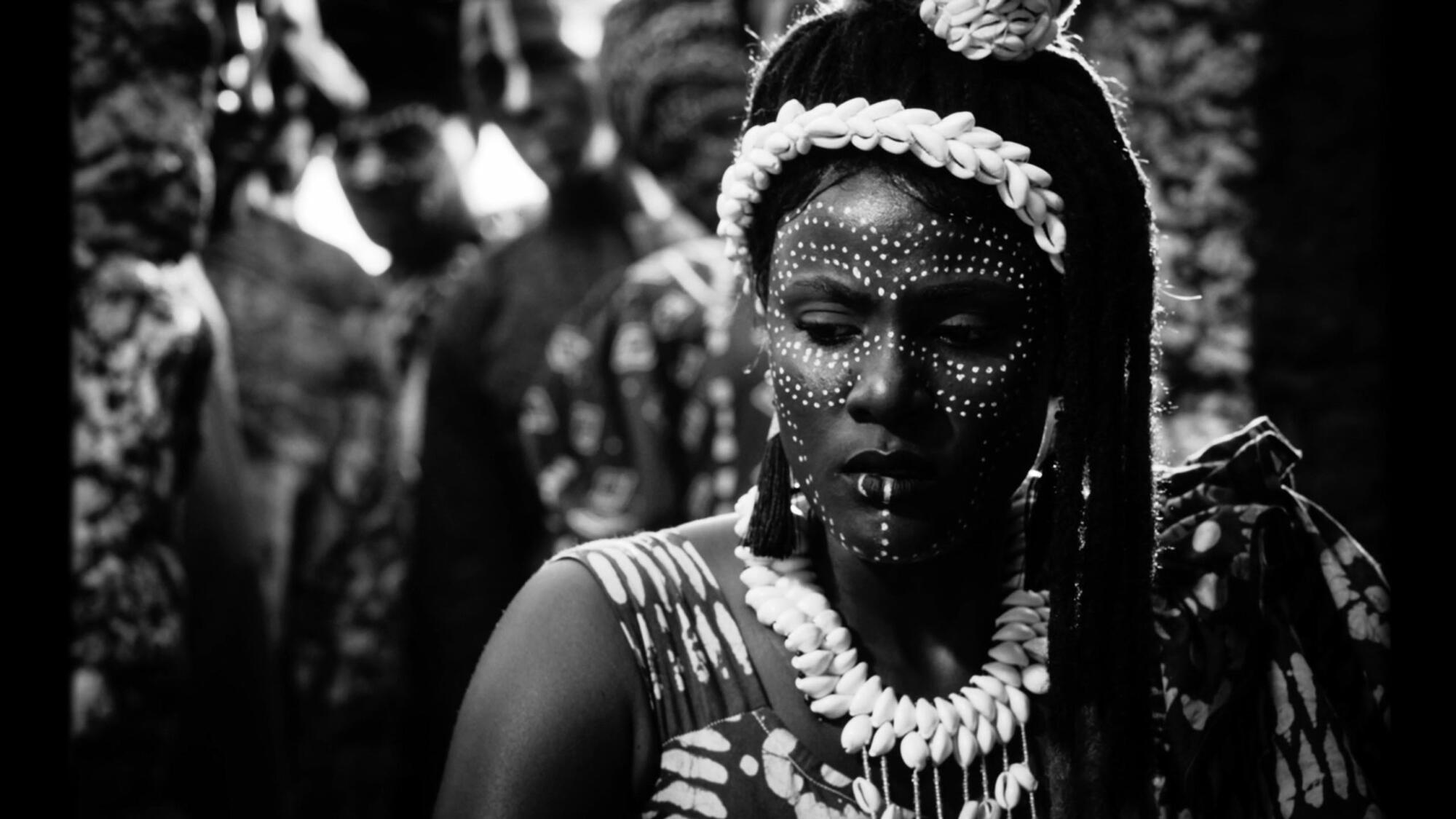 A black-and-white image of an African woman in face paint and cowrie shells.