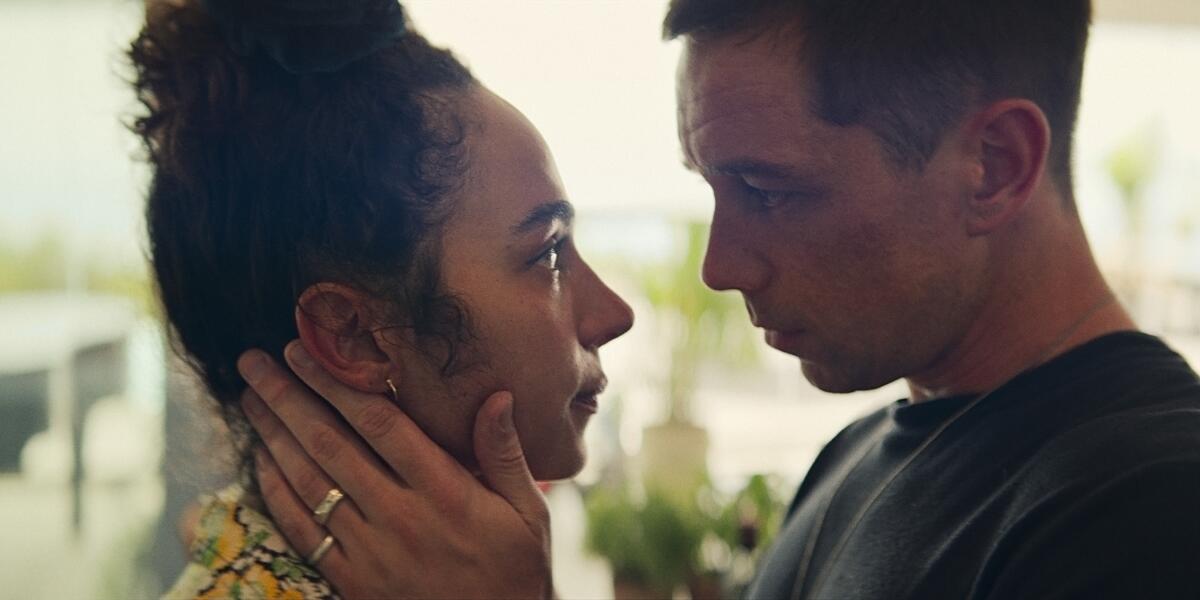 A woman looks at a man who has his hands on her neck.