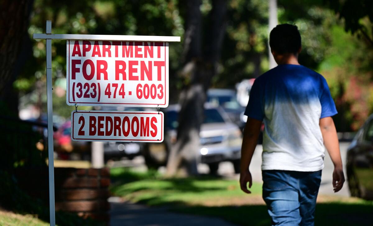 A person walks beside an apartment for rent sign