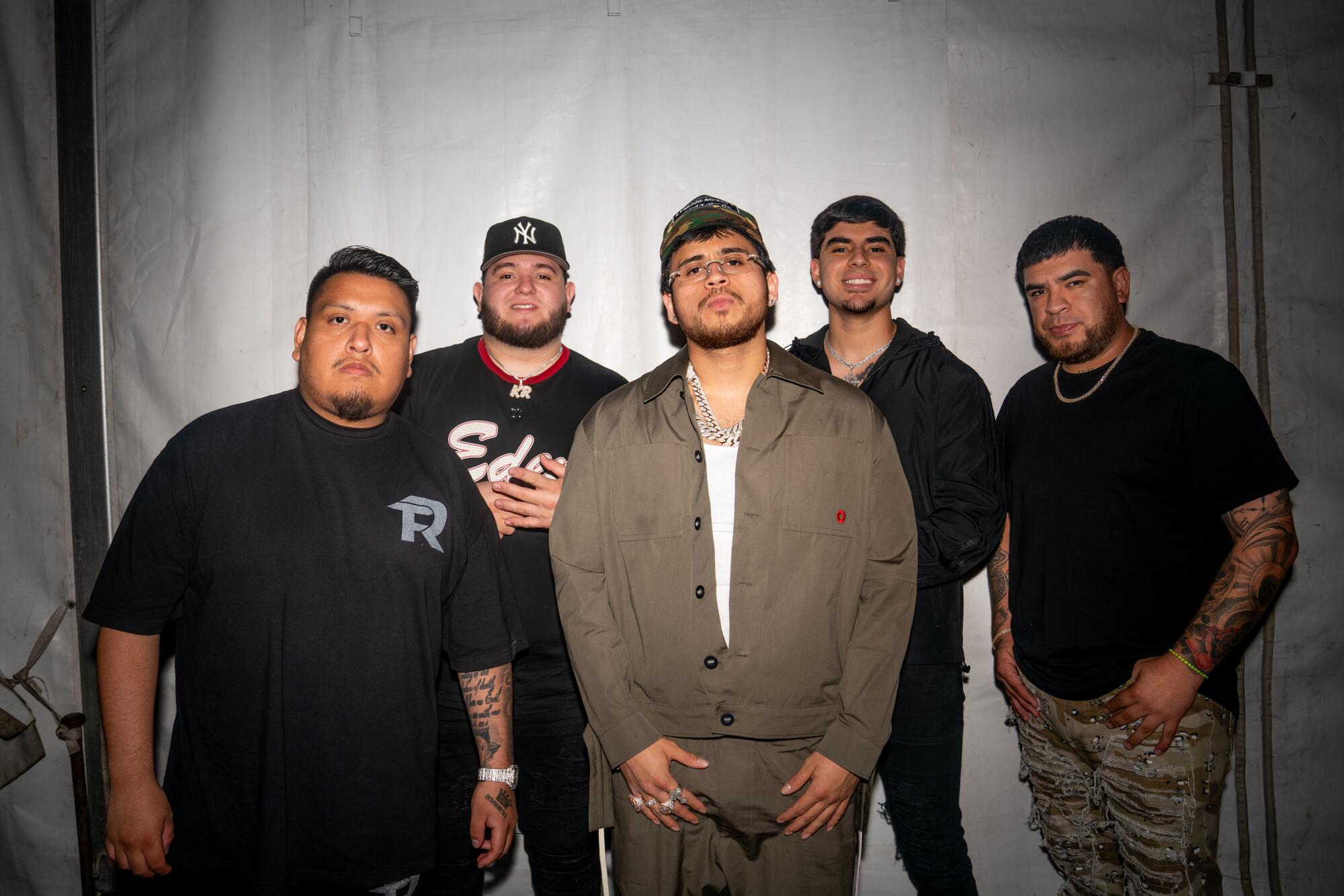 The five members of Fuerza Regida stand in a line, wearing dark casual clothes