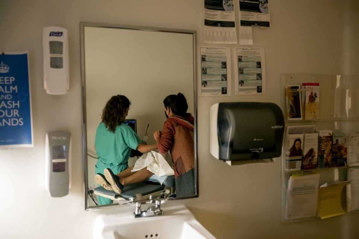 Two doctors reflected in a mirror perform an ultrasound on a patient.