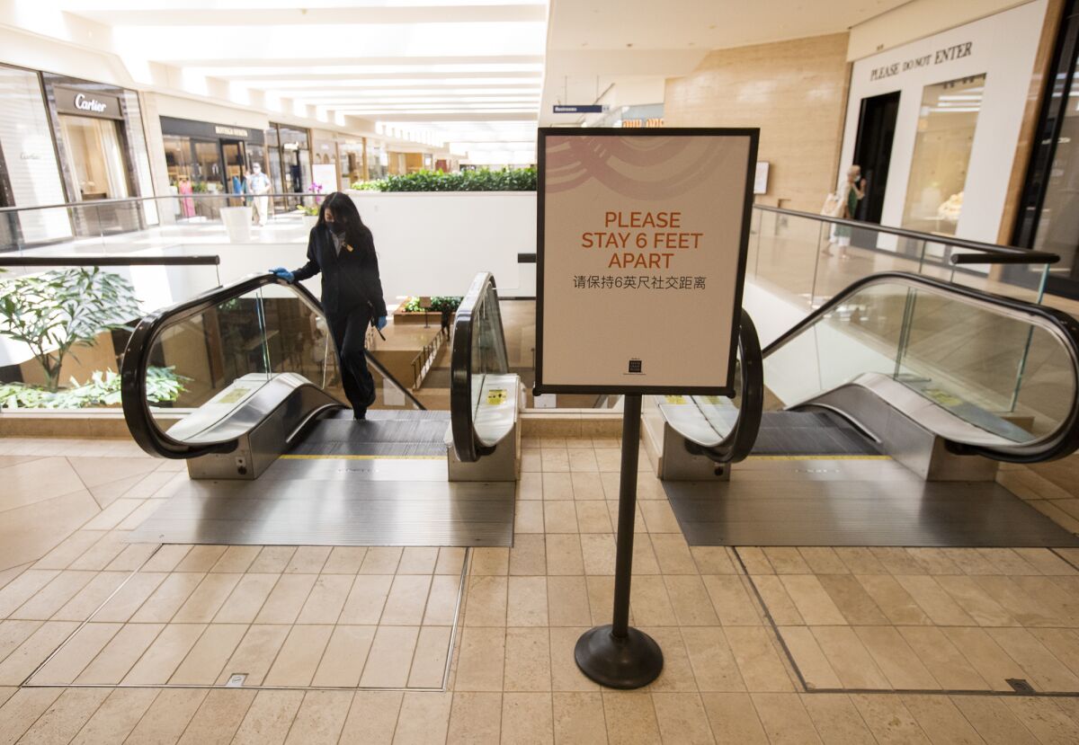 Signs asking customers to socially distance are spread throughout South Coast Plaza on Monday.
