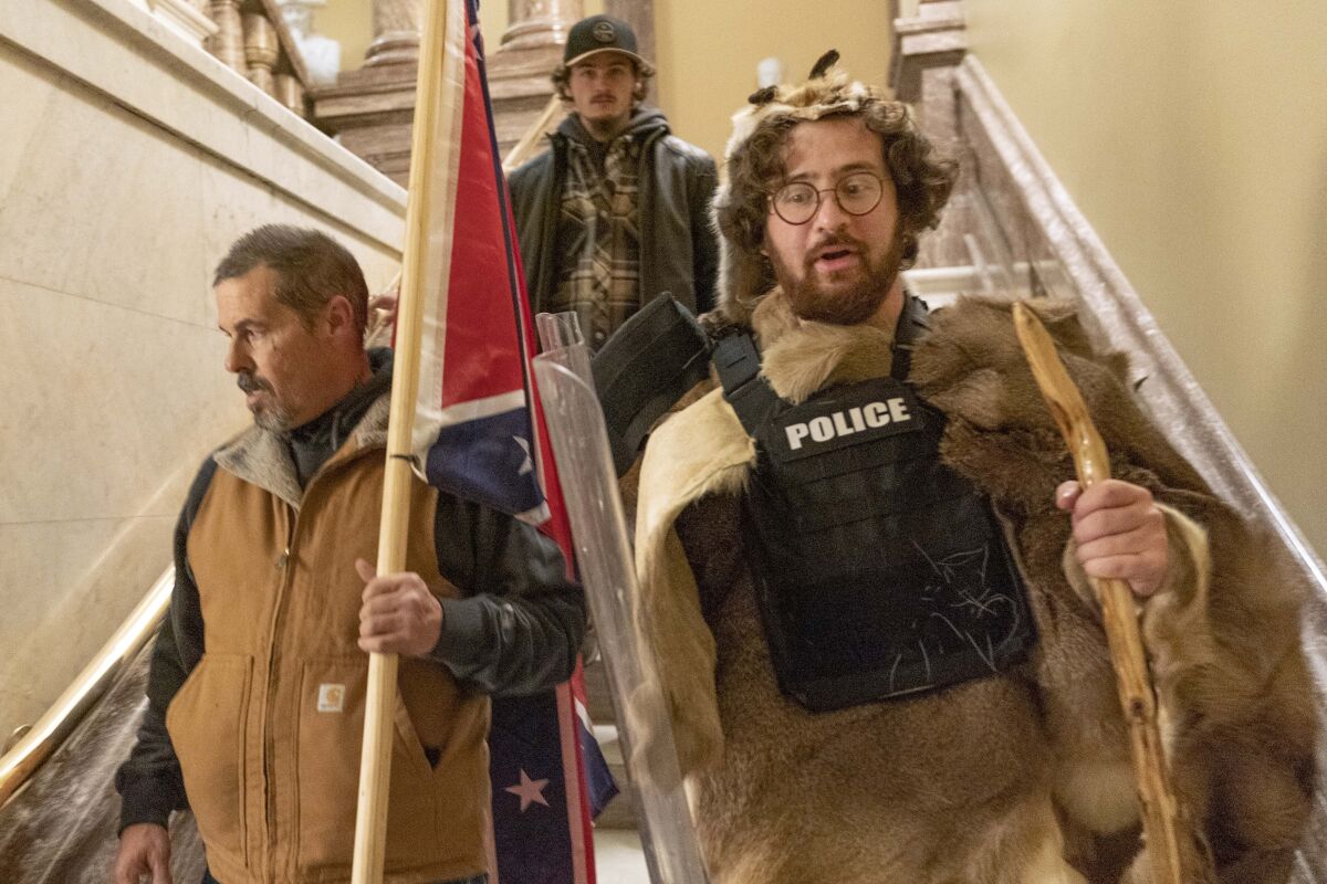 A man with a Confederate flag and another dressed in fur and using a walking stick descend a staircase.