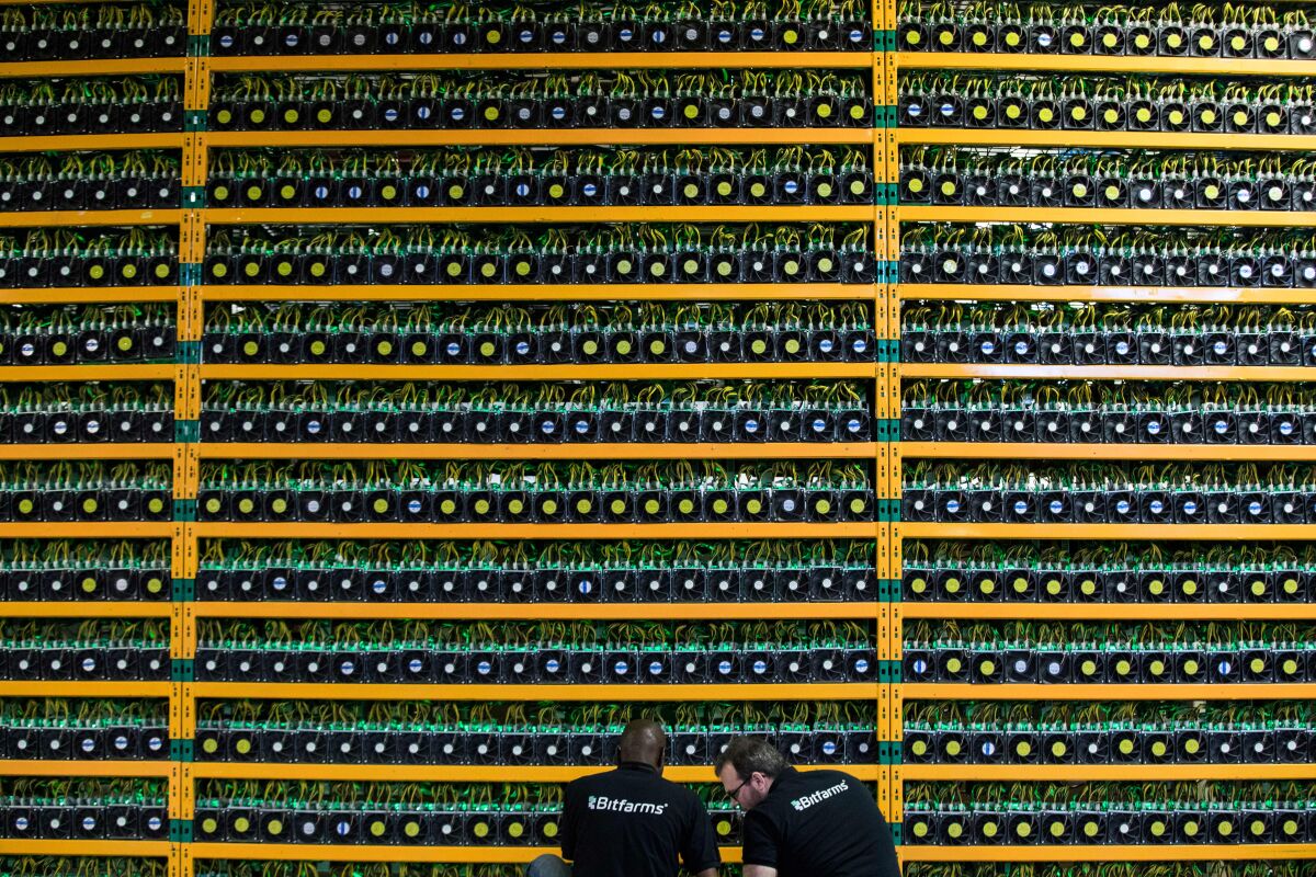 Two technicians inspect inspect rows of bitcoin mining 