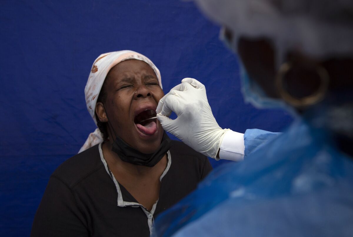A seated woman has her throat swabbed by a medical worker