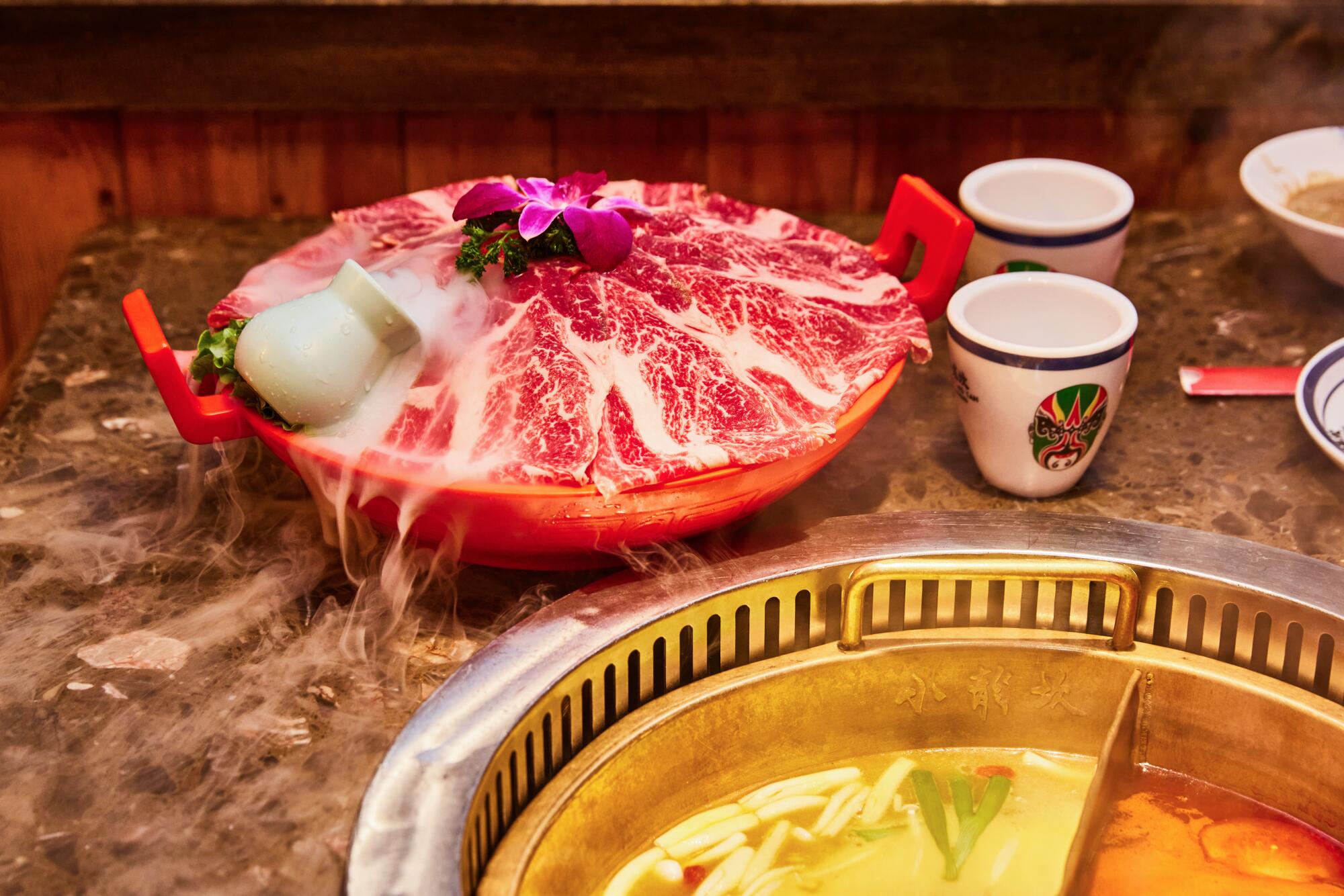Thinly sliced Wagyu beef on a mound of ice next to a metal pot full of hot broth