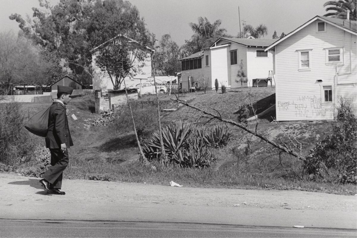 A black-and-white photograph shows a Mexican American soldier walking alone through a neighborhood