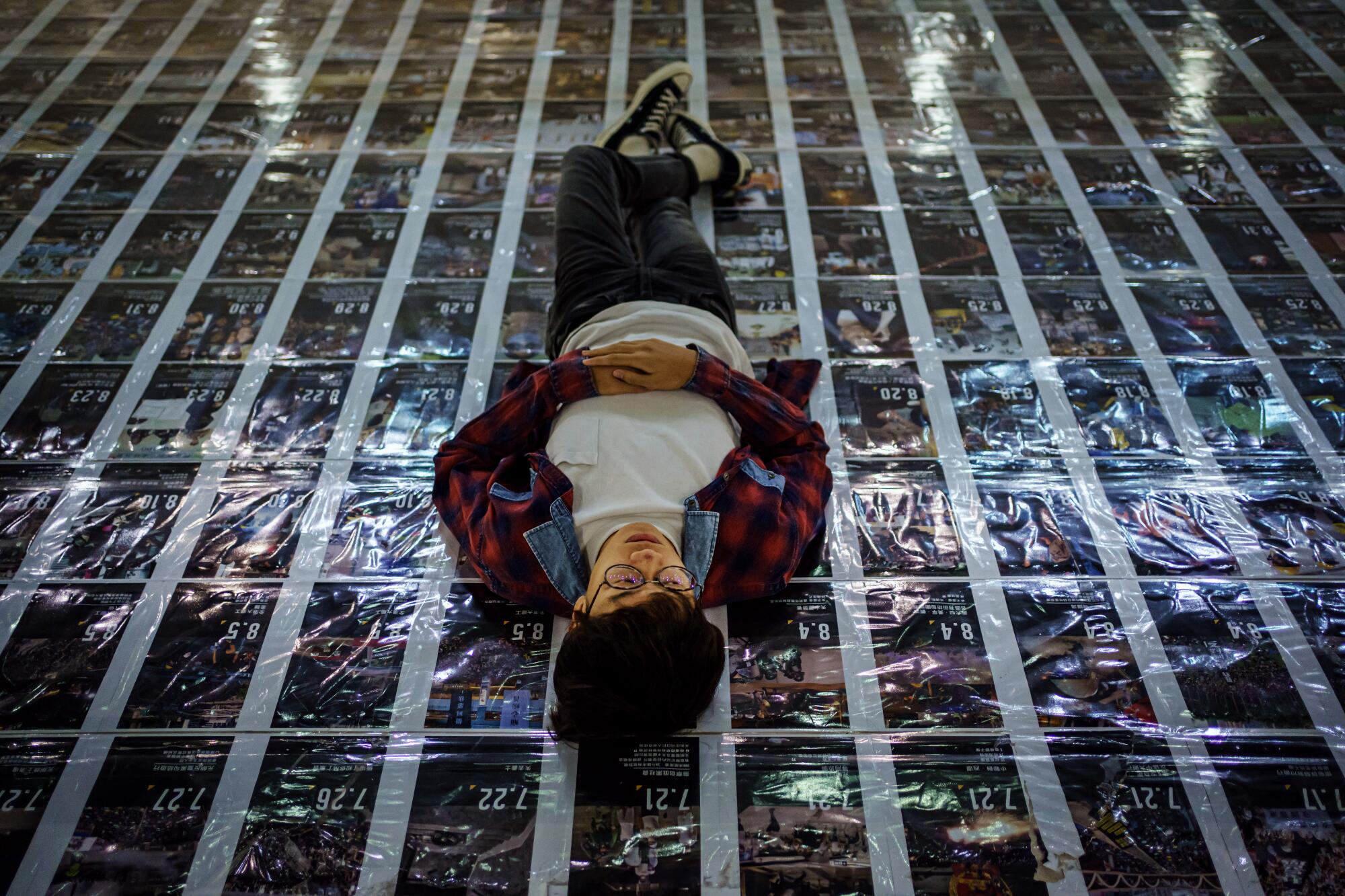 Ben Chan, a vocalist for the band Boyz Reborn, lies down on protest posters at his college.