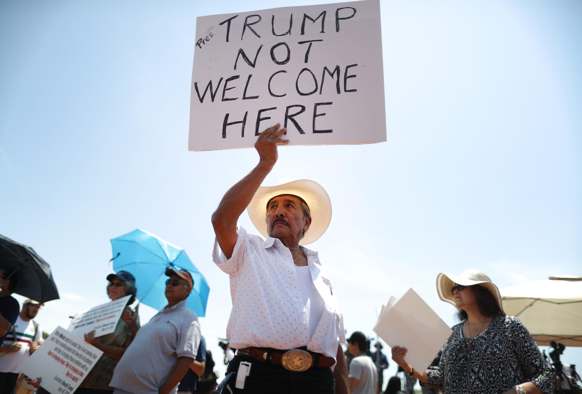 A man holds a sign saying "Trump not welcome here."