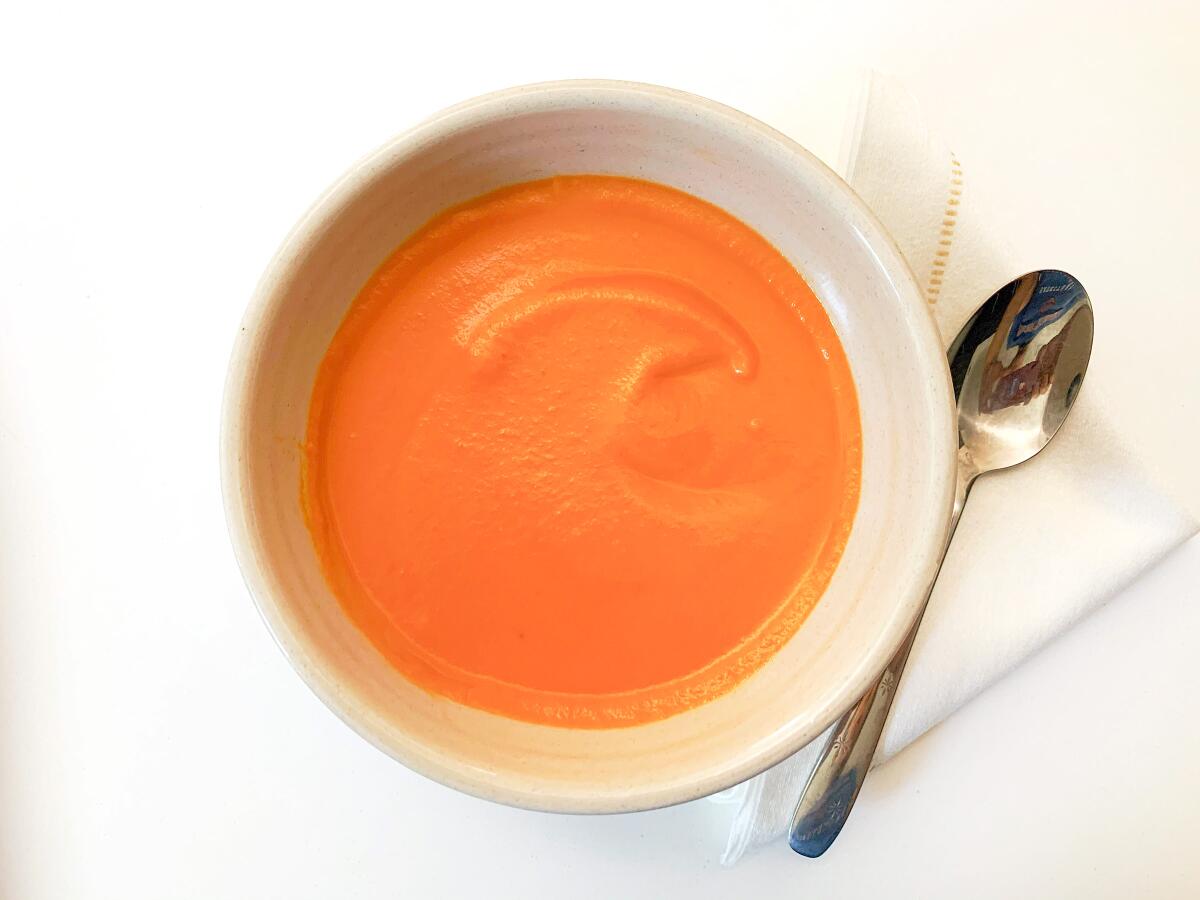 Closeup of a bowl of tomato soup on a white tablecloth.