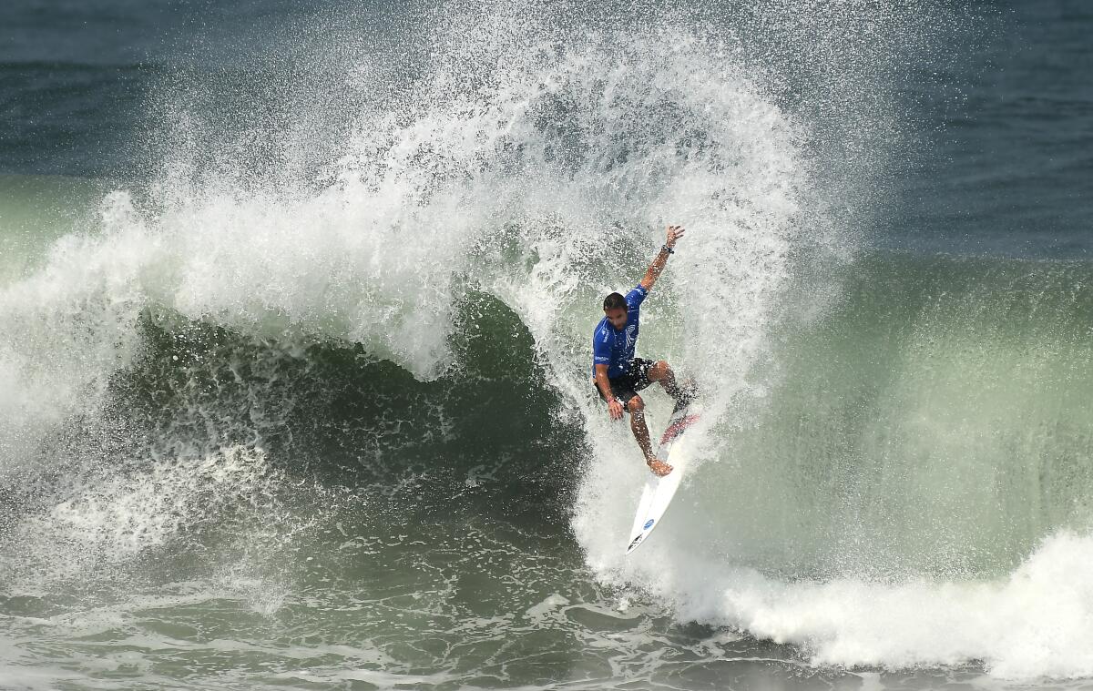 A surfer wearing blue rides a wave on a white board.