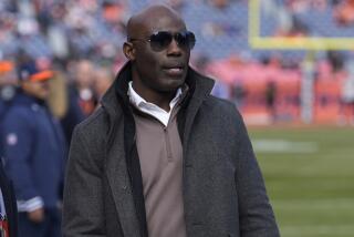 Terrell Davis wears sunglasses as he walks on the sideline before an NFL football game 
