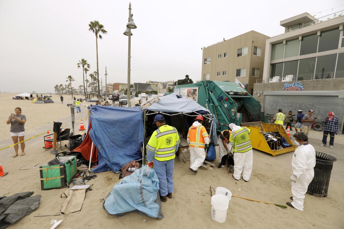 Workers stand outside makeshift tents on the beach with a sanitation truck nearby.