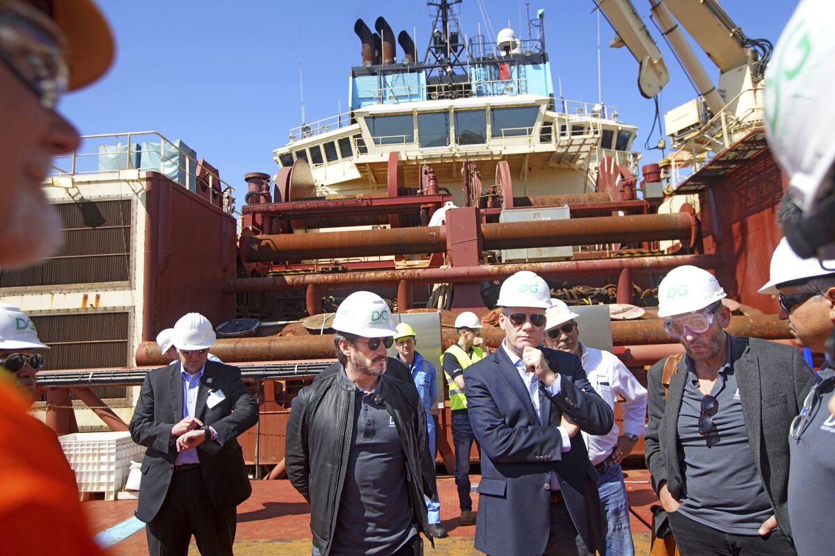 Men in hard hats stand in front of a massive ship at a dock. 