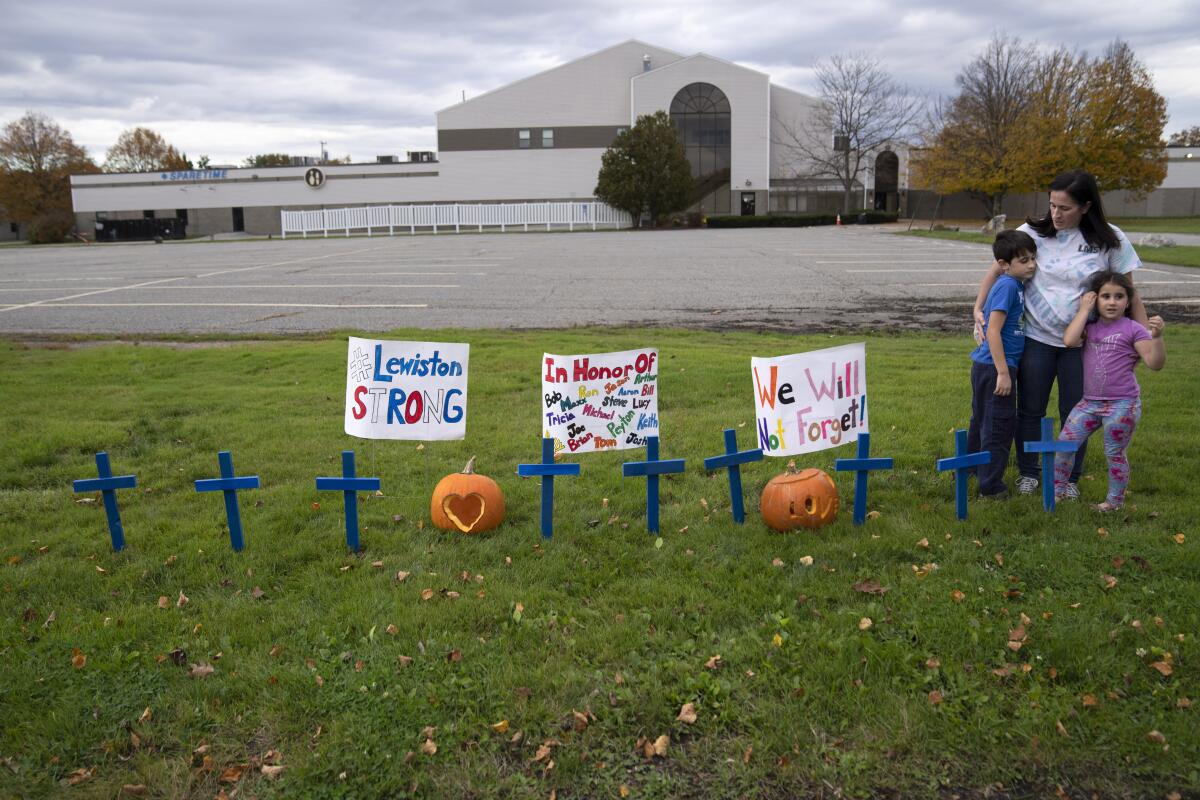 A woman stands with two small children near blue crosses and encouraging sings and two pumpkins in the grass.