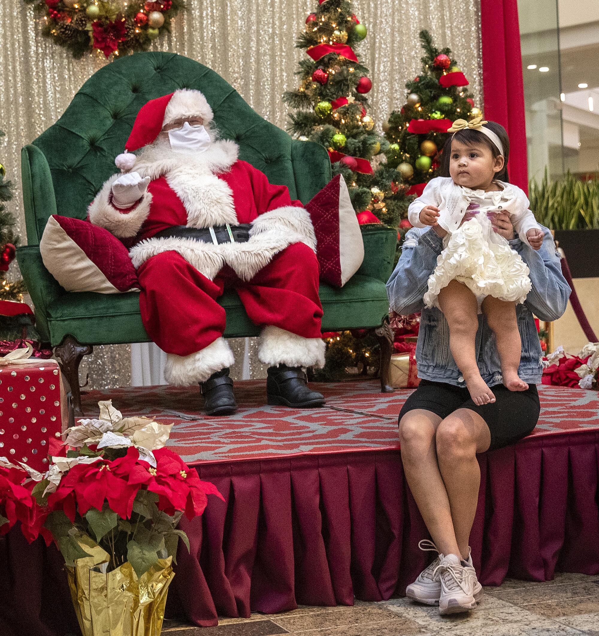 Aalie Godoy holds up her daughter, Alani Alvarez, 1, while being photographed in front of Santa Claus 