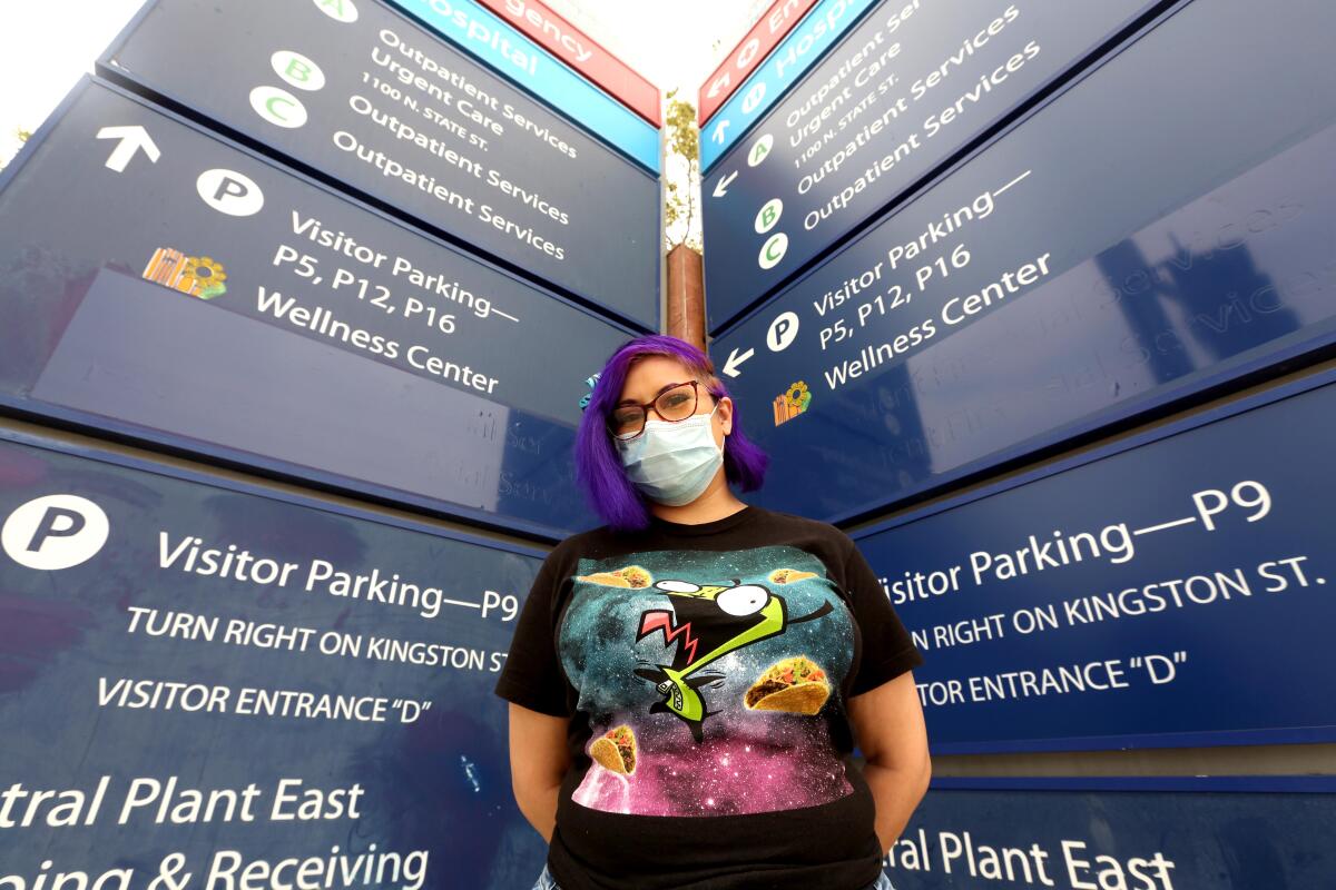 A person wearing a face mask stands between two columns of directional signs.