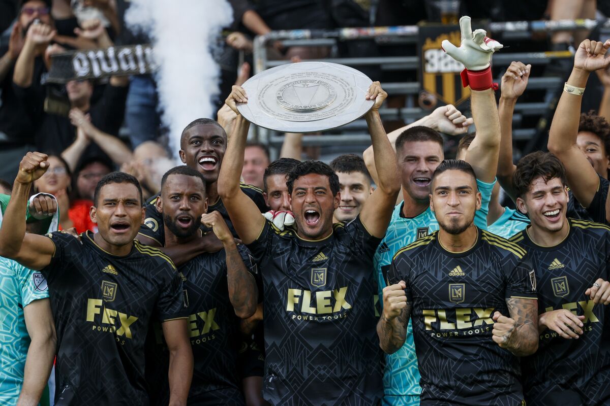 LAFC forward Carlos Vela, center, holds up the 2022 Supporters' Shield trophy while celebrating with his teammates