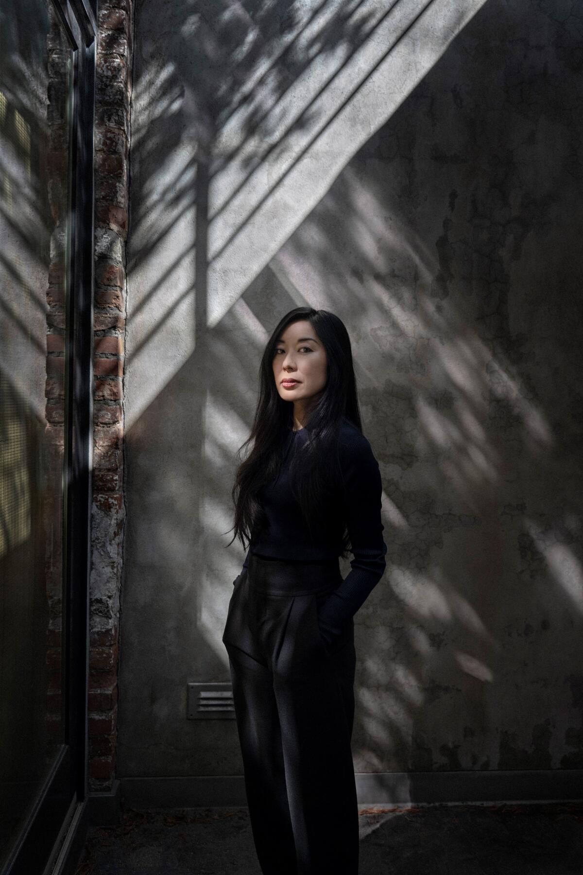 Author Katie Kitamura stands amid shadows.