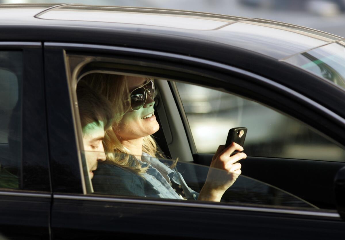 Una conductora parece estar enviando mensajes de texto, mientras maneja su auto en la intersección del bulevar Santa Mónica y Wilshire, en el Sur de California.