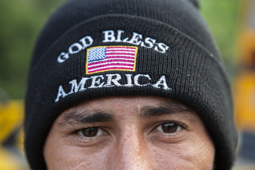 Un migrante hondureño que trató de llegar a la frontera entre México y Estados Unidos mira a cámara con un gorro de lana con la frase en inglés "Dios bendiga a Estados Unidos", tras ser detenido y deportado a su país, en Copán, Honduras, el 20 de enero de 2021. Tras un año de parálisis provocado por la pandemia, quienes están en contacto diario con los migrantes creen que el flujo migratorio hacia el norte podría regresar a los niveles récord vistos a finales de 2018 y principios de 2019. (AP Foto/Oliver de Ros)