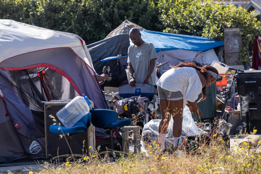 Los Angeles, CA - June 26: Thomas Richardson, left, and cousin Tatayana Noles, right, gather up belongings in a tent encampment on 86th and Broadway where Inside Safe initiative employees got them a place to stay Wednesday June 26, 2024 in Los Angeles, CA. (Brian van der Brug / Los Angeles Times)