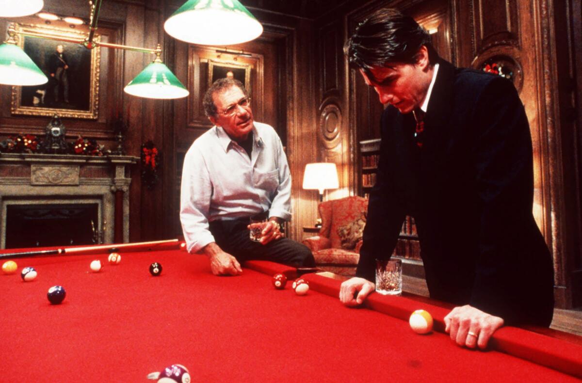 Two men have a discussion around a red pool table.