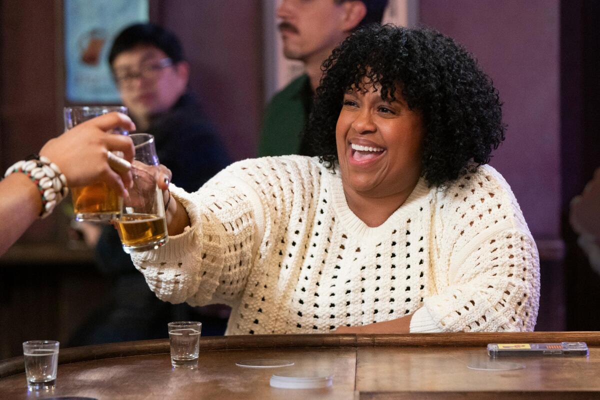 A curly-haired woman in a white sweater toasts with a glass.