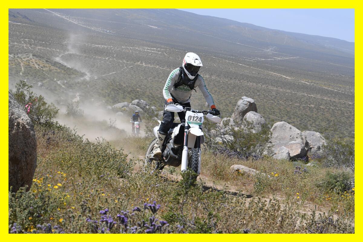 A helmeted man on a dirt bike riding through a desert landscape