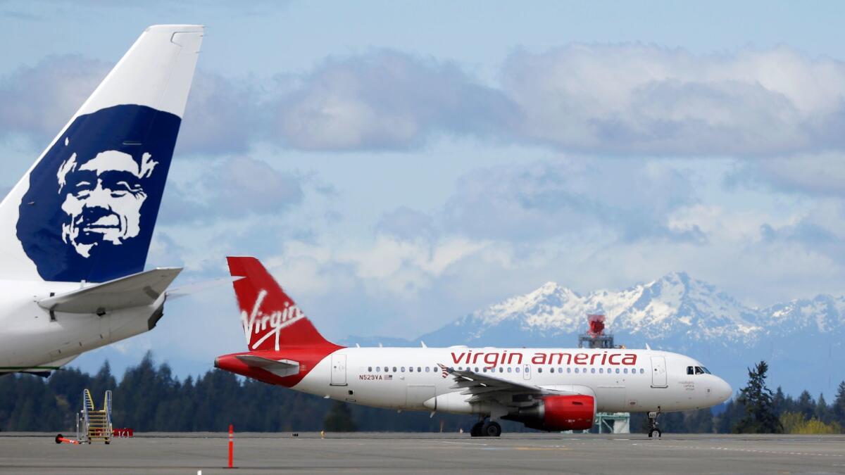 A Virgin America plane taxis past an Alaska Airlines plane waiting at a gate at Seattle-Tacoma International Airport in 2016. Alaska Airlines acquired Virgin America last year and announced plans to retire the Virgin America name.