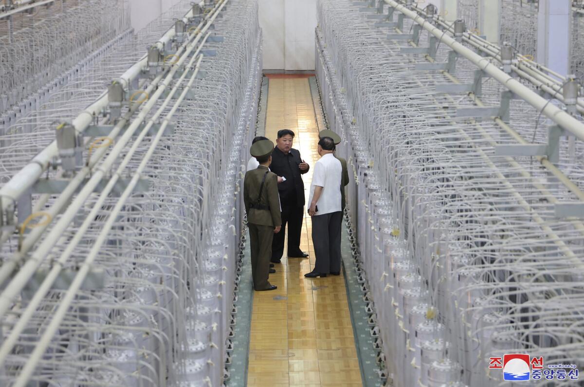 An overhead view of Kim Jong Un standing between two rows of gray tubes talking to other men