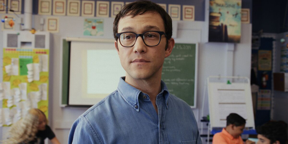 A teacher wearing glasses and a denim shirt in his fifth-grade classroom