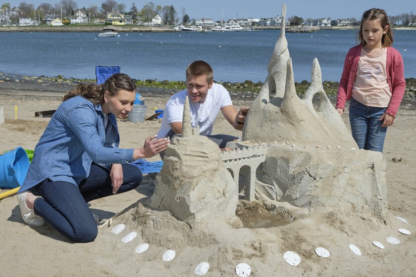 A woman, a man and a girl build a sand castle surrounded by sand dollars