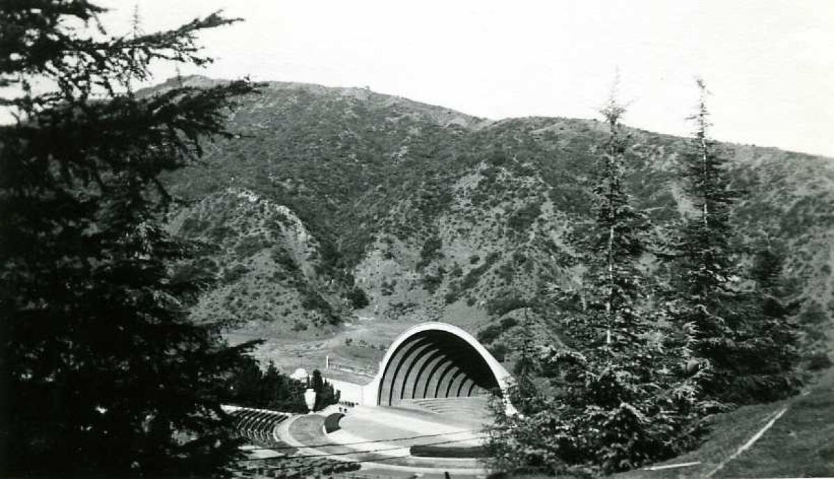 A black and white image shows an empty outdoor amphitheater tucked into a rustic hillside.