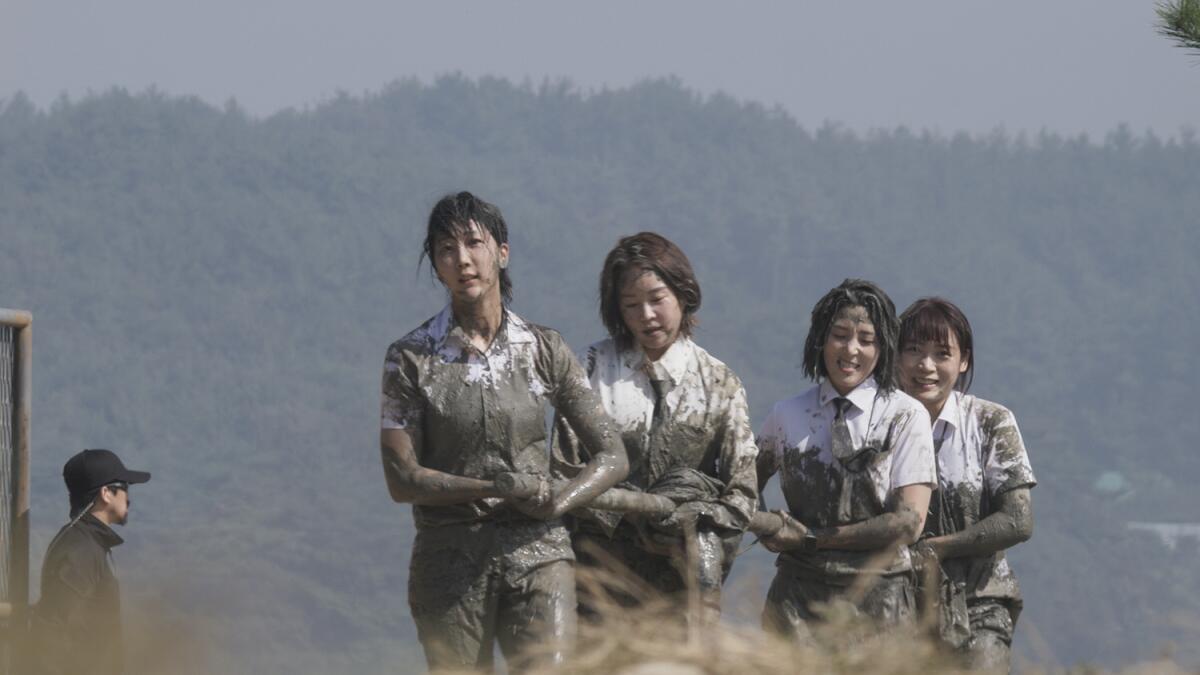 Four women in white outfits, covered up to their torsos in mud