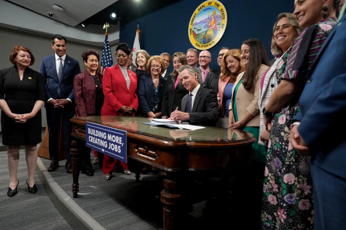California Gov. Gavin Newsom signs documents at a desk while several people watch.