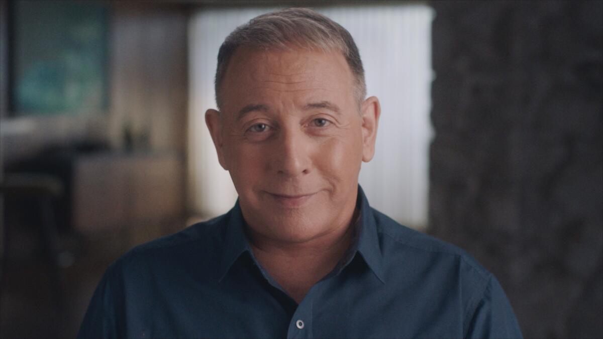 A man in a blue shirt smiling slightly as he looks directly forward.