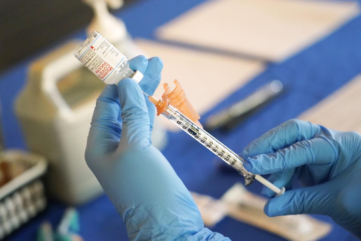 A nurse prepares a syringe of a COVID-19 vaccine at an inoculation station.