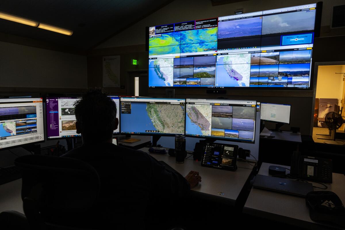 A person looks over an array of computer screens that depict wildfire camera systems. 