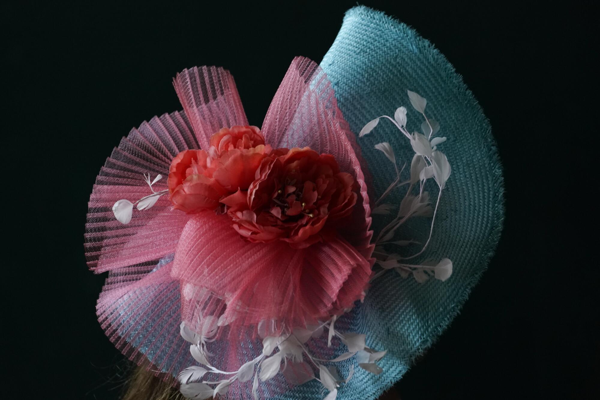 A woman wears a light blue hat with a cloth red rose on it. 