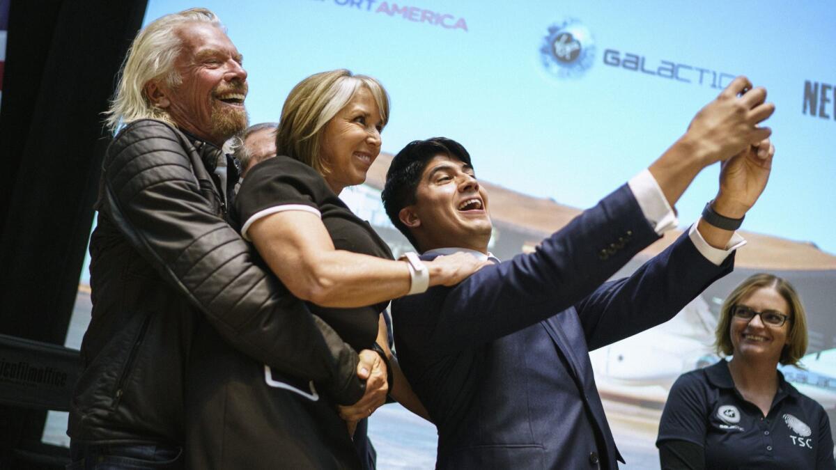 Virgin Galactic founder Richard Branson picks up New Mexico Gov. Michelle Lujan Grisham while company employee Kevin Prieto takes a selfie with them at an event Friday in Santa Fe.