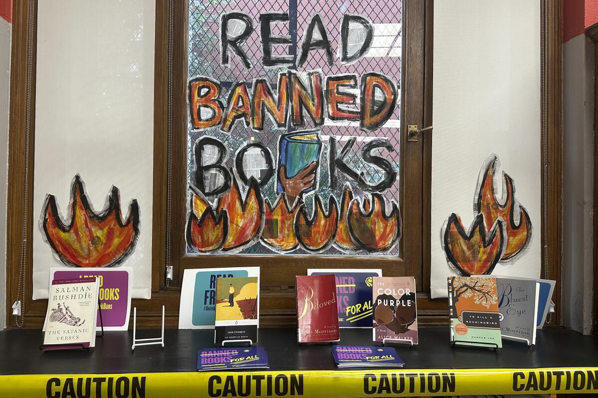 A Banned Books Week display includes books and caution tape in front of a window painted with flames.
