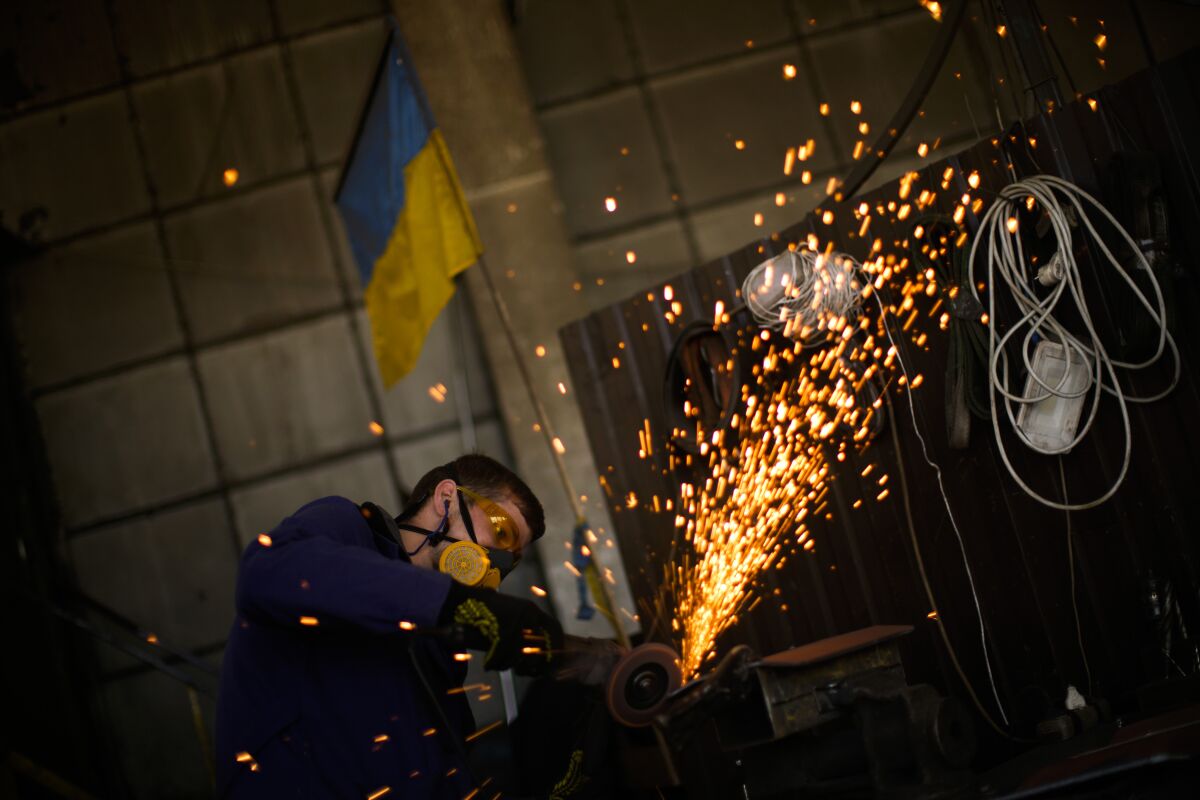 A volunteer shapes metal plates with an angle grinder at a facility producing material for Ukrainian soldiers in Zaporizhzhia, Ukraine, Saturday, May 7, 2022. An old industrial complex in the southeastern Ukrainian riverside city of Zaporizhzhia has become a hive of activity for volunteers producing everything from body armor to camouflage nets, anti-tank obstacles to heating stoves and rifle slings for Ukrainian soldiers fighting the Russian invasion. (AP Photo/Francisco Seco)
