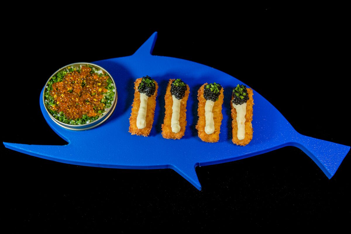Fish sticks dotted with caviar are served with seven-layer dip on a blue fish-shaped platter