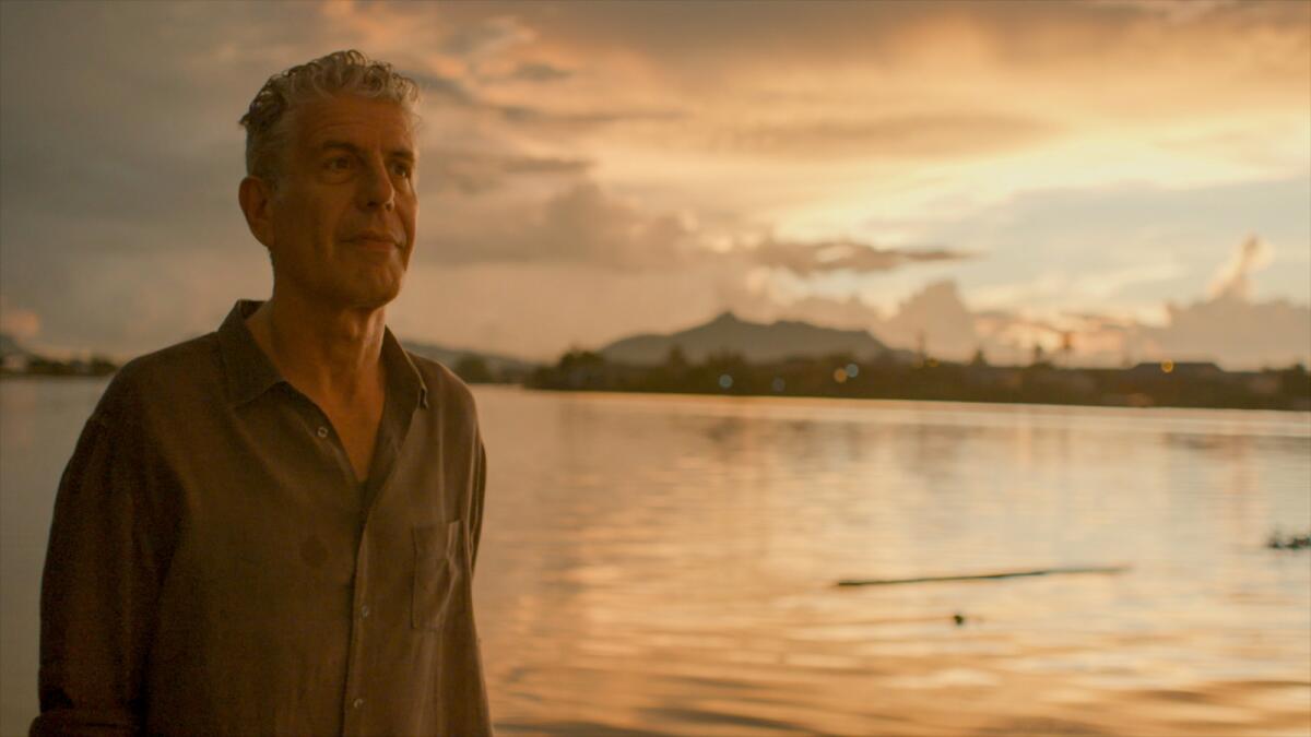 A man in a button-down shirt stands by a lake at sundown