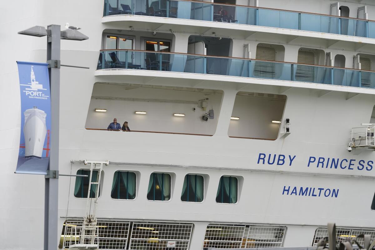 Two people stand on a rear balcony of a cruise ship