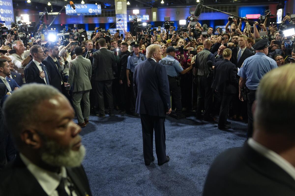 Former President Trump stands alone in a crowded room.