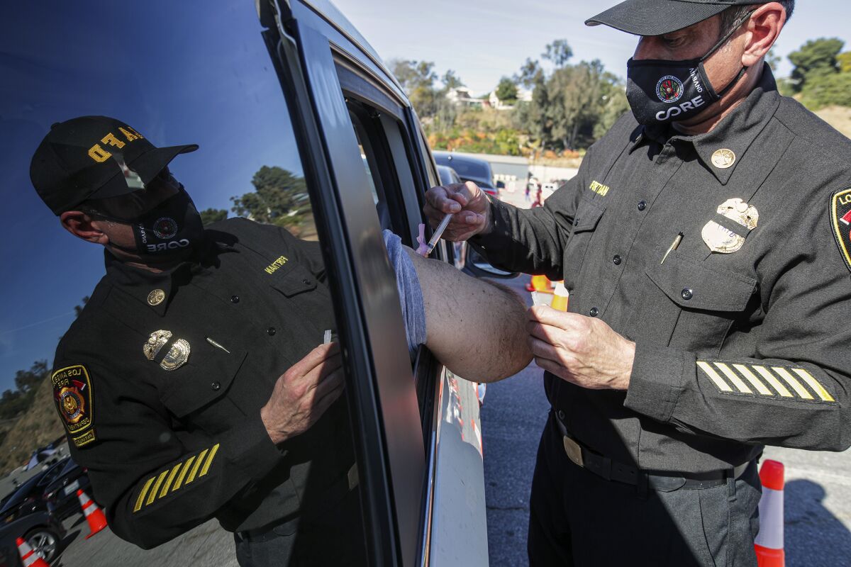 A man in an LAFD uniform gives an injection to a passenger in a vehicle.